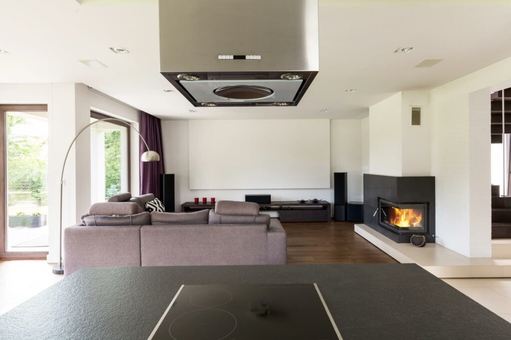 Agencement de salon avec canapé en L séparant stratégiquement le coin multimédia et l'espace cheminée.