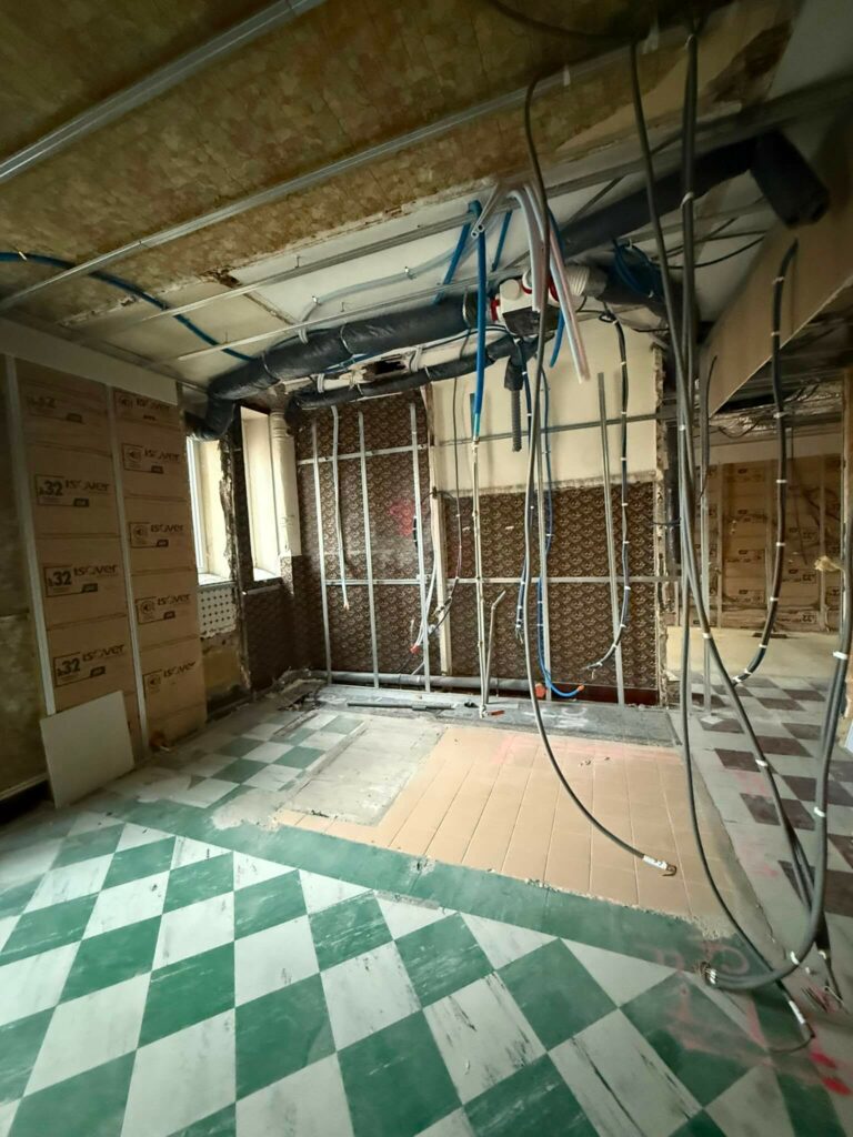 Ancien papier peint et réseaux électriques/plomberie apparents avant la reprise complète du logement